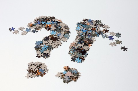 A question mark and an exclamation mark made from jigsaw puzzle pieces, next to each other, dissolving on the white background.