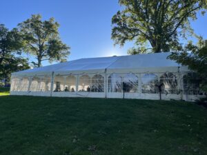 marquis tent with clear plastic sides among trees and blue sky on a sunny day